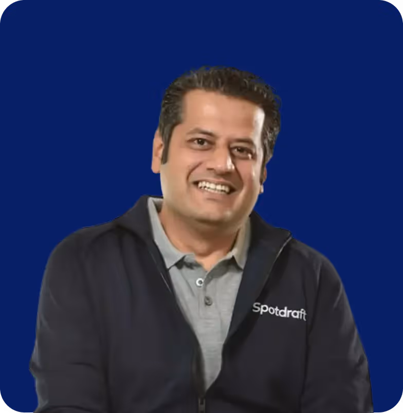 Smiling man wearing a navy Spotdraft jacket over a gray polo shirt, against a dark blue background.