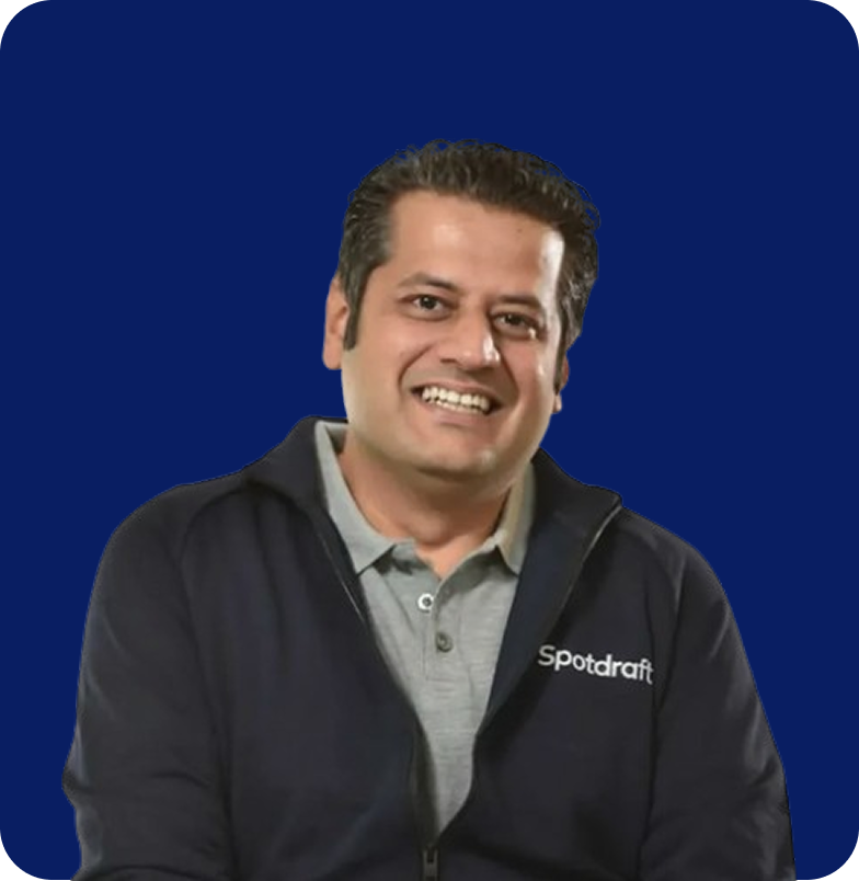 Smiling man wearing a navy Spotdraft jacket over a gray polo shirt, against a dark blue background.