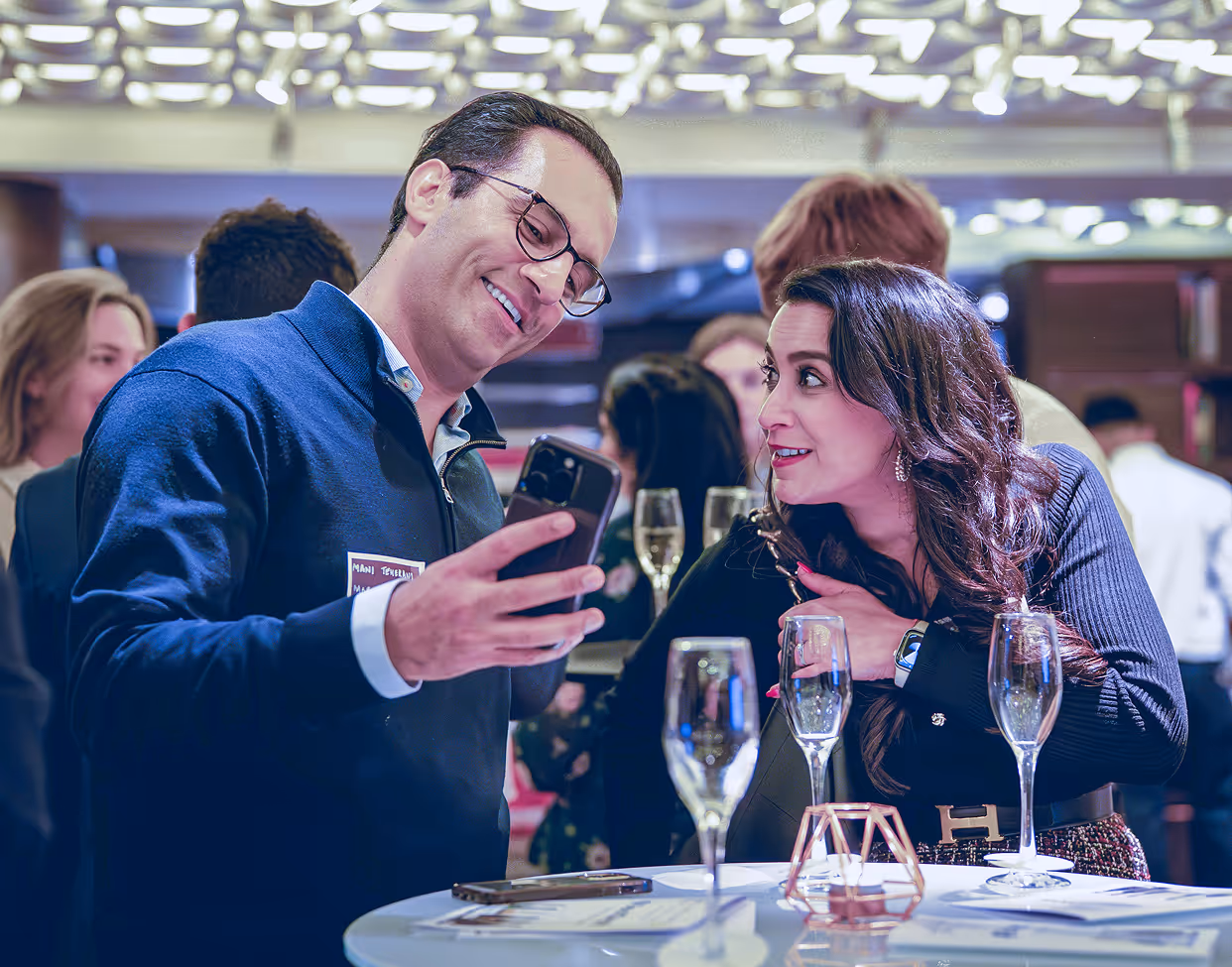 Man showing a smartphone to a woman at a social event with glasses of champagne on the table.