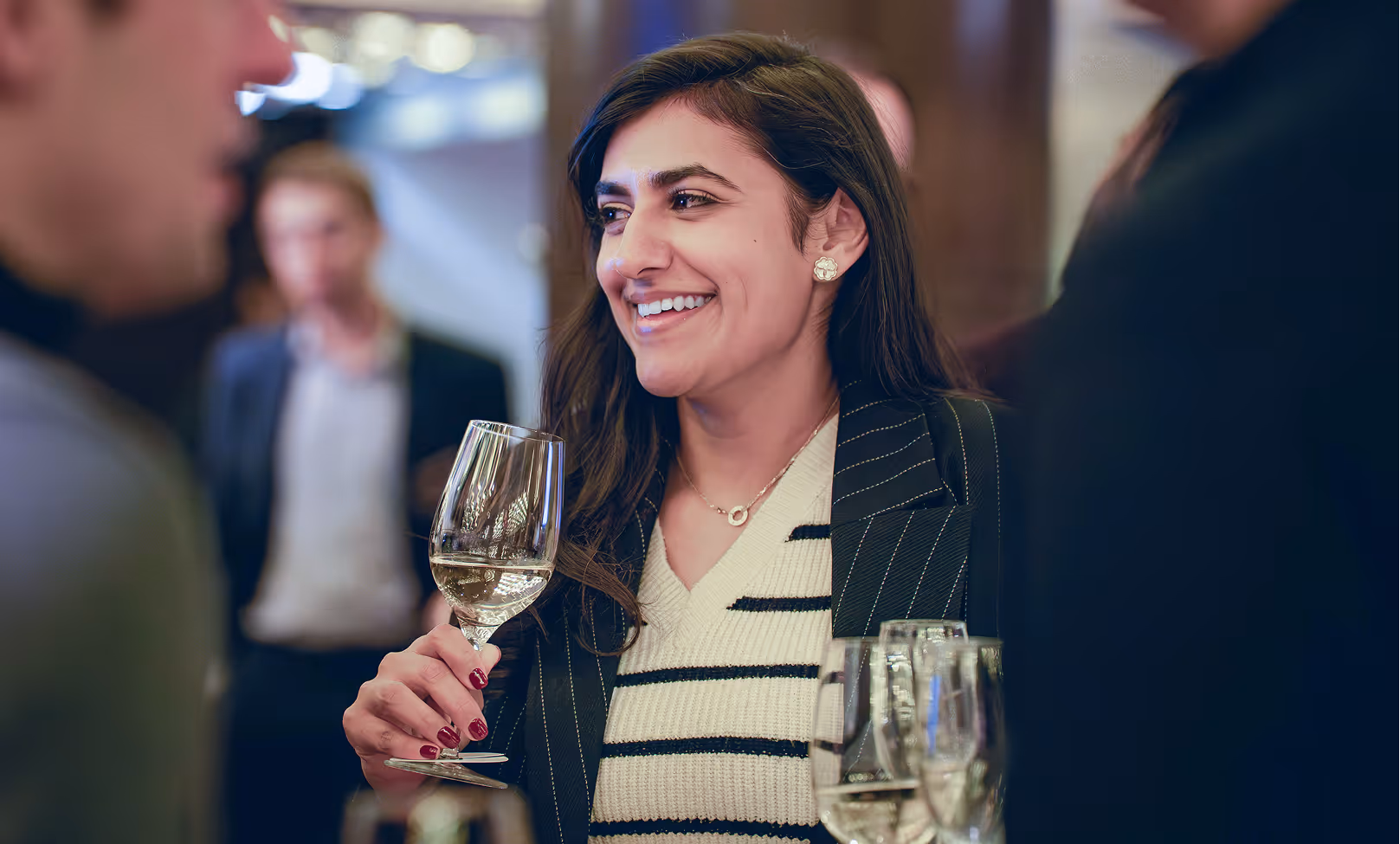 Smiling woman holding a glass of white wine at a social gathering.