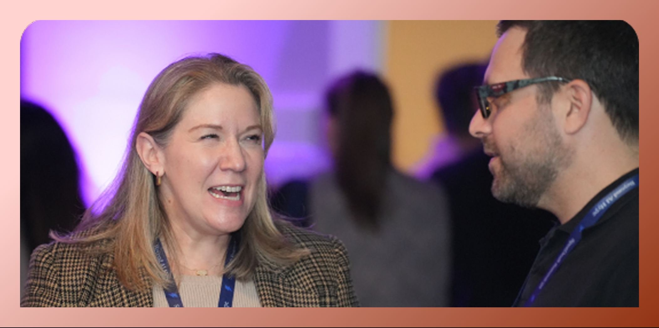 Two people engaged in a lively conversation at an indoor event with purple lighting in the background.