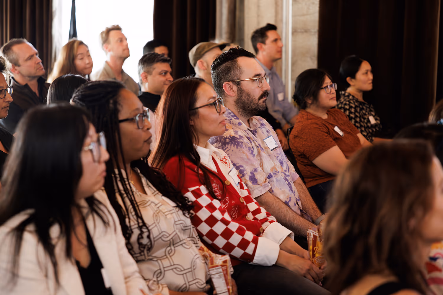 A diverse group of adults seated indoors attentively listening to a presentation or lecture.