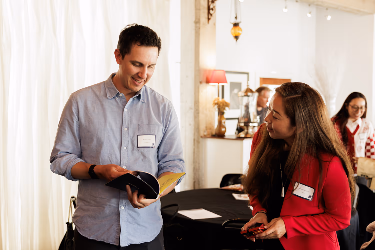 Two people smiling and looking at a booklet together in a warmly lit indoor setting.