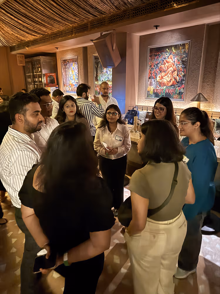 A group of people standing in a warmly lit room having a conversation.