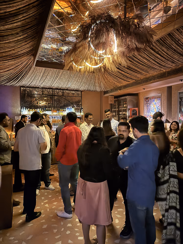 People socializing inside a warmly lit bar with a decorated ceiling and illuminated bar shelves.