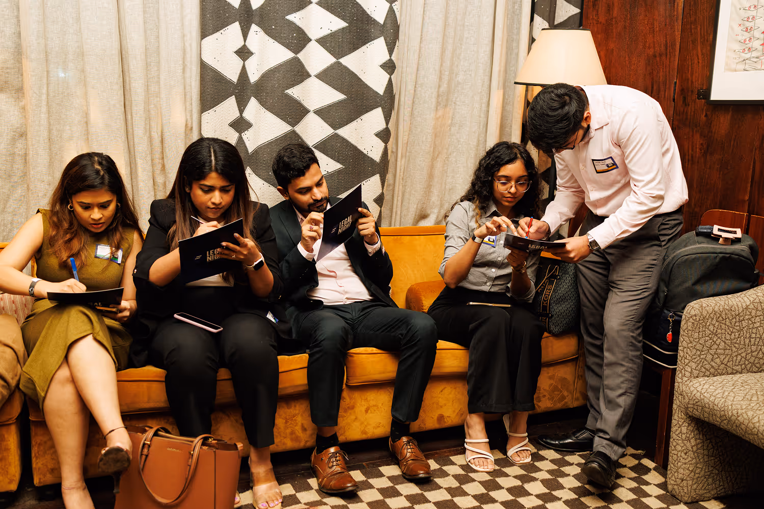 Five professionals seated on a couch, focused on writing in notebooks labeled 'Legal Night'.