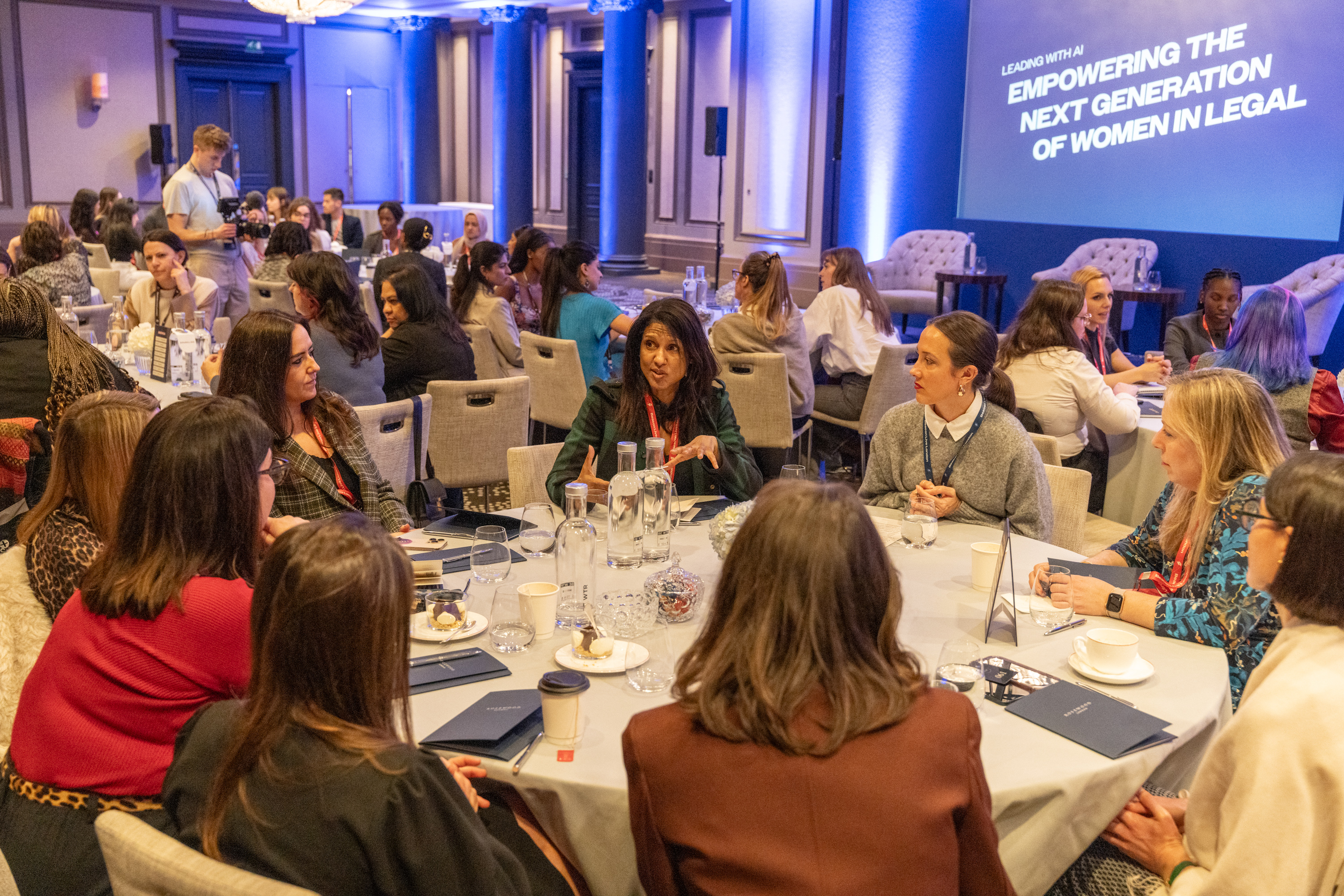 Attendees discussing at a roundtable event with a projection screen titled Empowering the Next Generation of Women in Legal