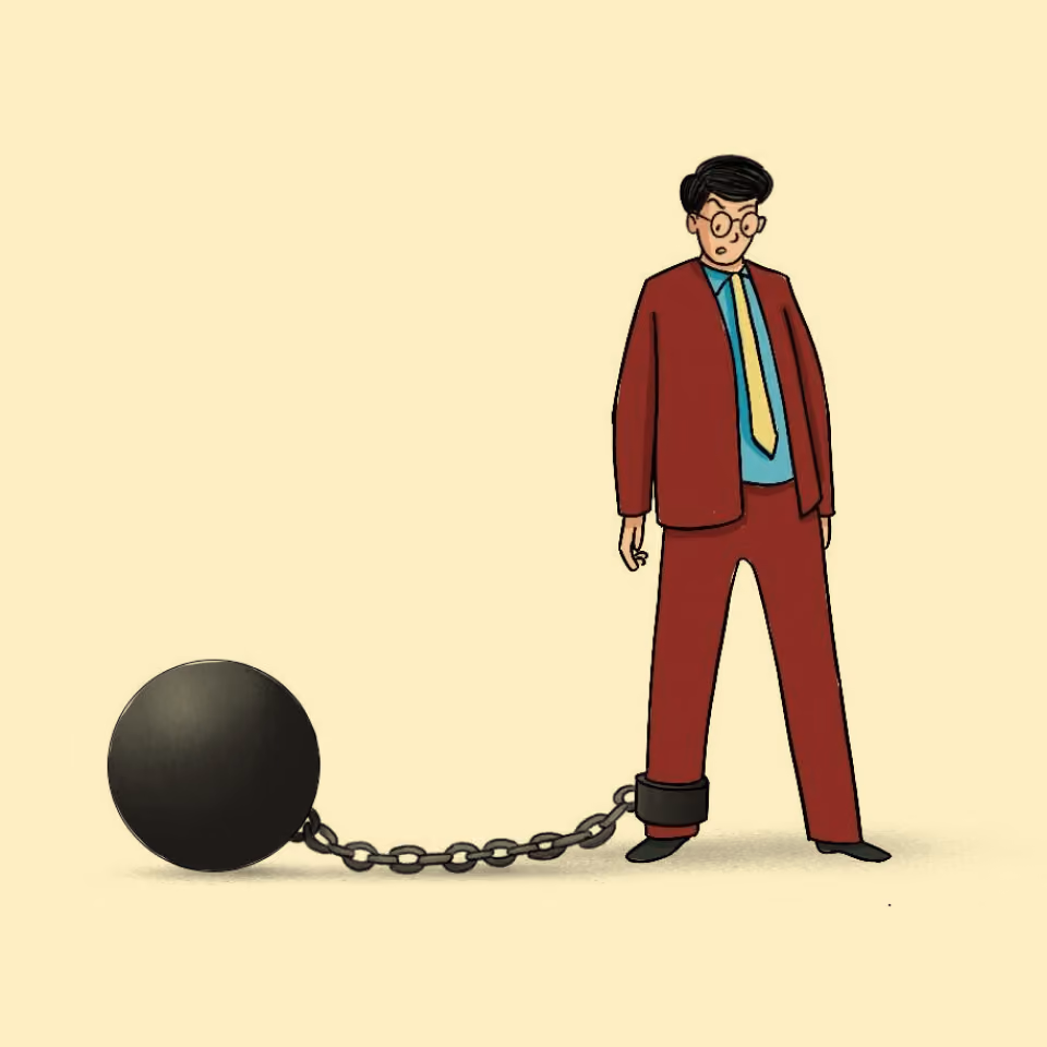 Man in red suit with yellow tie chained by the ankle to a heavy black ball.
