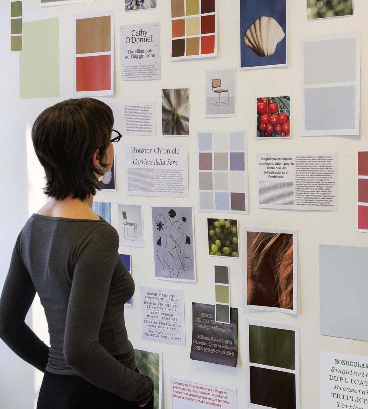 Emily Stevens, graphic designer looking at moodboard on wall.