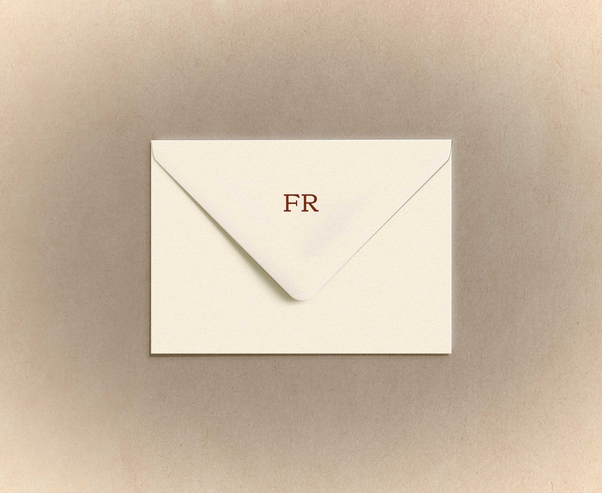 Cream-colored envelope with the letters 'FR' printed on the flap, placed on a light brown textured surface.