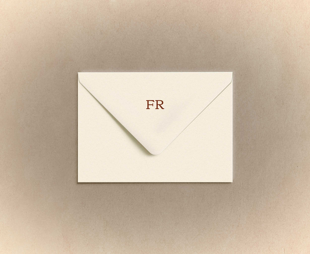 Cream-colored envelope with the letters 'FR' printed on the flap, placed on a light brown textured surface.
