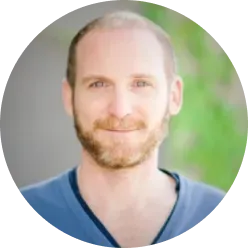 Portrait of a smiling man with a light beard and short hair against a blurred green background.