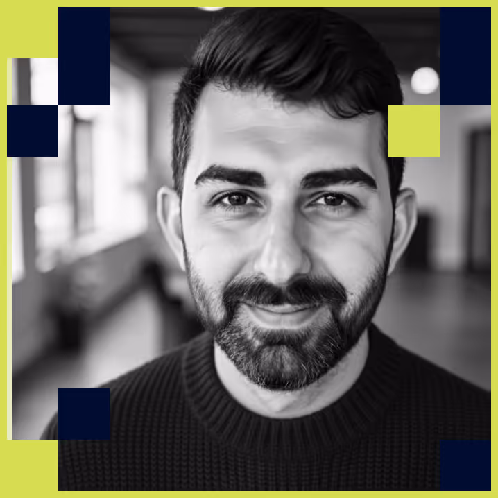 Black and white portrait of a smiling bearded man with short hair wearing a knit sweater in an indoor setting.