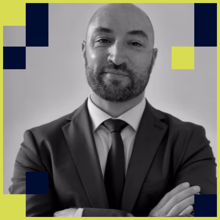 Portrait of a bald man with a beard wearing a suit and tie, standing with arms crossed.