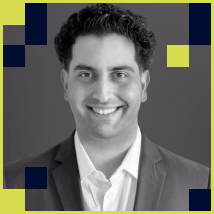Smiling man with dark curly hair wearing a suit jacket and white shirt against a gray background with yellow and dark blue geometric shapes.