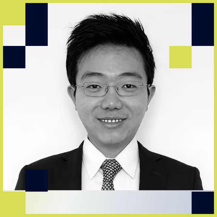 Portrait of a smiling man wearing glasses, a suit, and a patterned tie against a white background with decorative green and blue squares.
