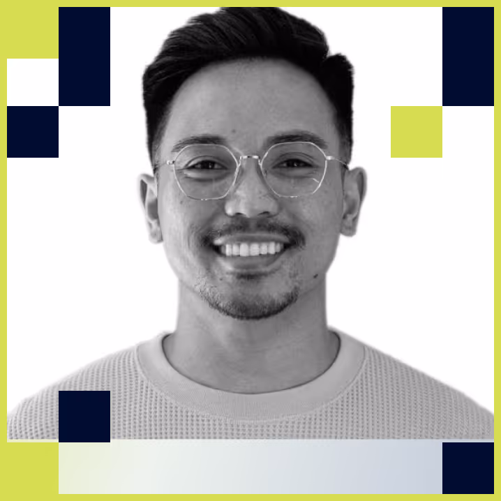 Smiling young man with short dark hair and glasses wearing a light sweater.