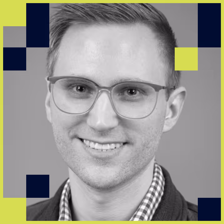 Smiling man with short hair and glasses wearing a checkered shirt and jacket, against a plain background with decorative squares.