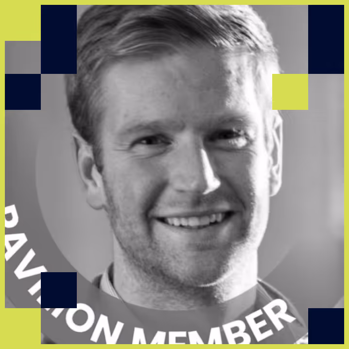 Black and white headshot of a smiling young man with short hair against a background with text partially showing 'PAVILION MEMBER'.