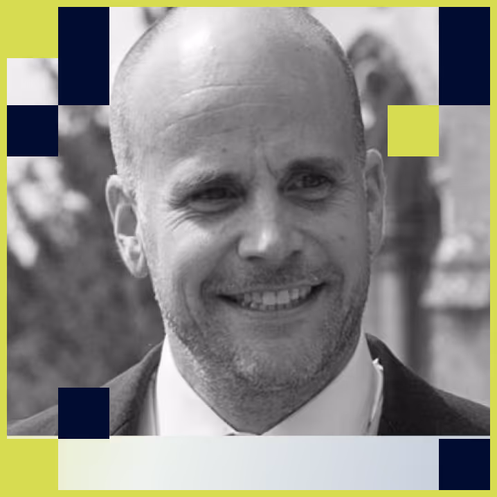 Portrait of a smiling bald man with a beard wearing a suit and tie, with abstract squares framing the image.