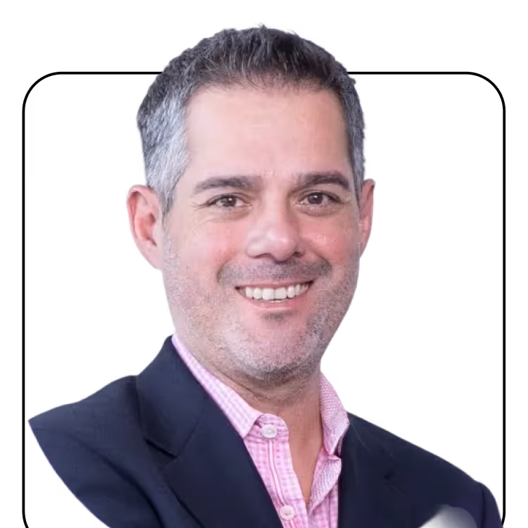 Smiling man with short gray hair wearing a pink checkered shirt and dark blazer.