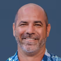 Smiling middle-aged man with a bald head and gray beard wearing a blue patterned shirt.