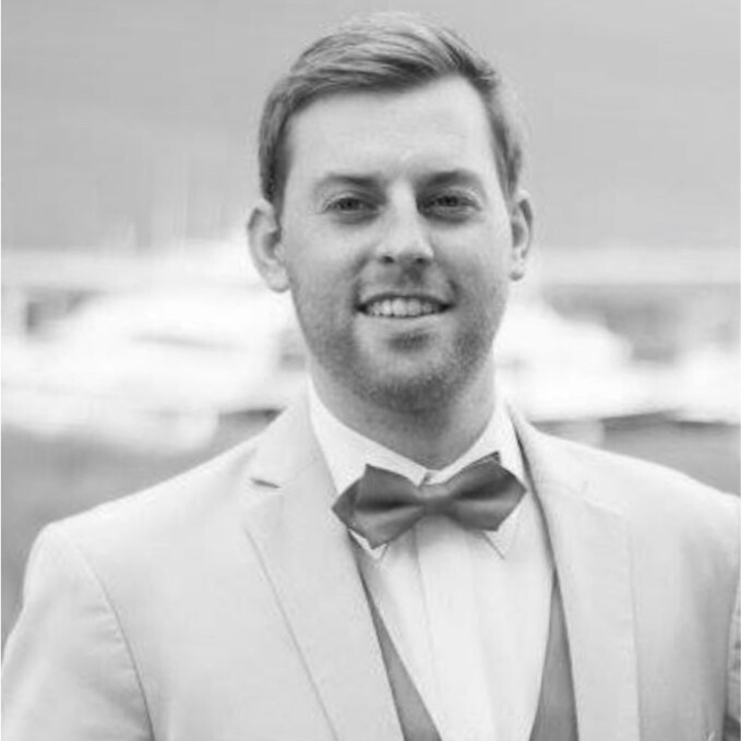 Portrait of a smiling man in a light suit jacket and bow tie with blurred outdoor background.