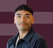 Portrait of a young man with short black hair wearing a dark collared shirt against a maroon background.