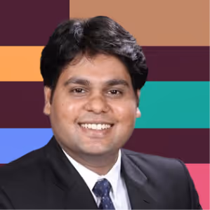 Smiling man with dark hair wearing a black suit and blue tie, color block background.