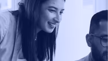 Smiling woman with long dark hair leaning over a man wearing glasses.