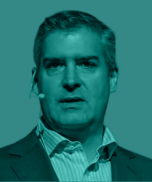 Man with gray hair wearing a headset microphone and a suit jacket over a striped shirt.