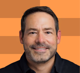 Smiling man with short dark hair and beard wearing a black shirt on an orange background.