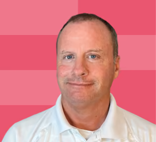 Smiling middle-aged man with short hair wearing a white collared shirt on a pink striped background.