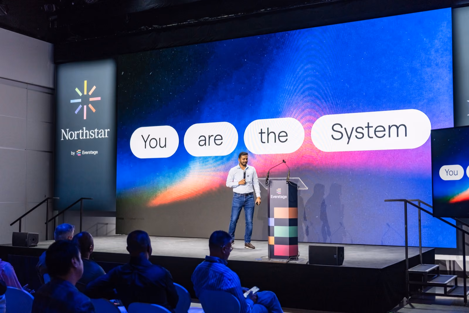 Siva Rajamani on stage at Northstar '26 in front of a screen reading 'You are the System'
