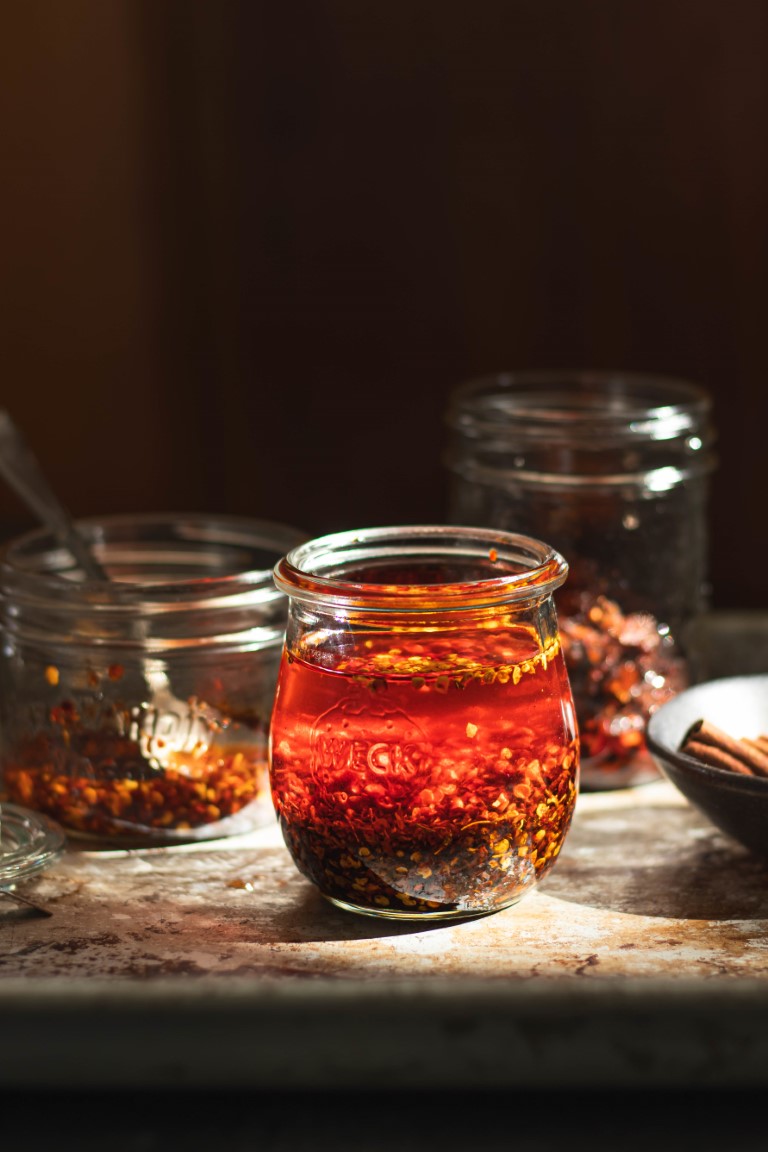 Glass bottle filled with Sichuan garlic chili oil surrounded by additional bottles and a bowl of spices