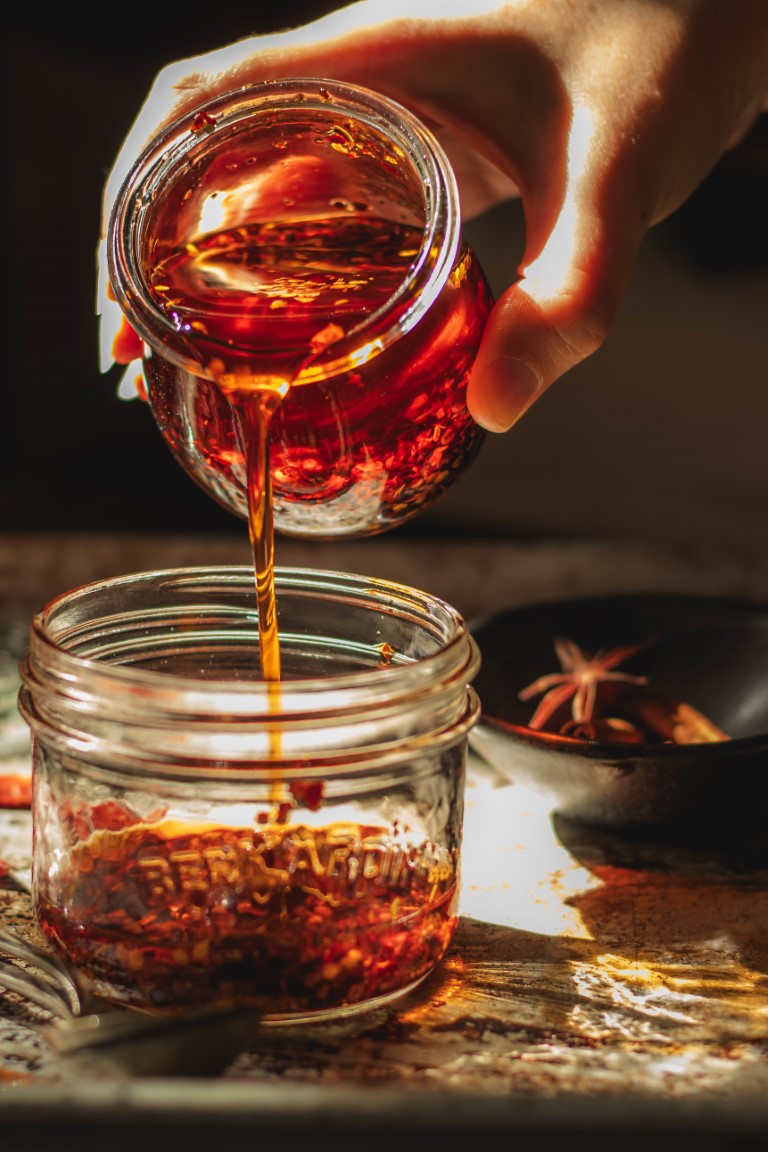 Woman's hand pouring a jar of Sichuan chili oil into another jar of chili oil