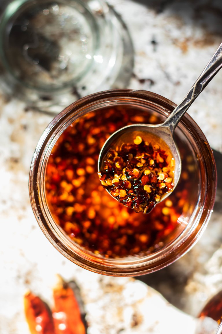 A spoon of red chili flakes spooned out of a jar of Sichuan garlic chli oil