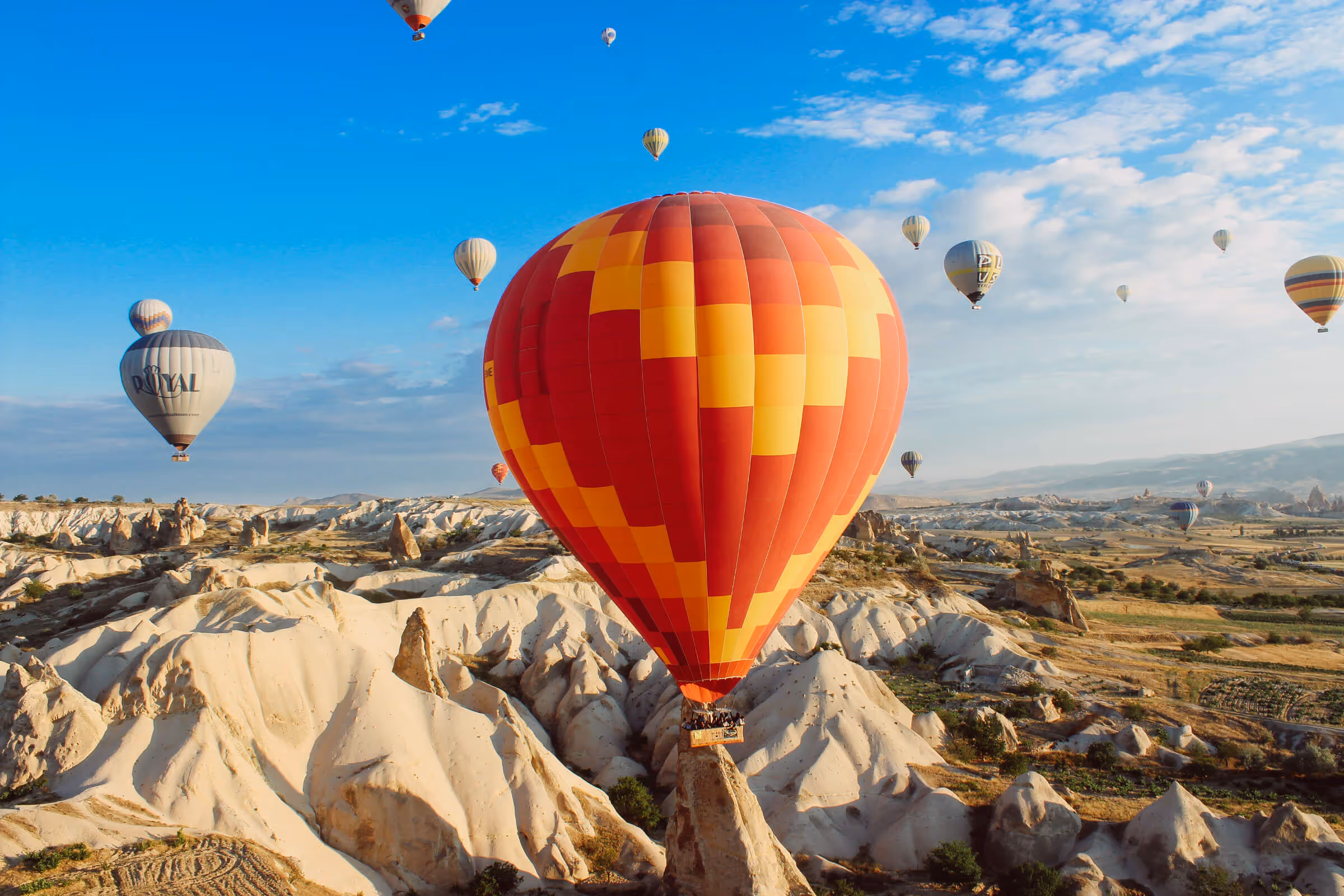 Colorful hot air balloons floating over a rocky, desert landscape under a blue sky with scattered clouds.