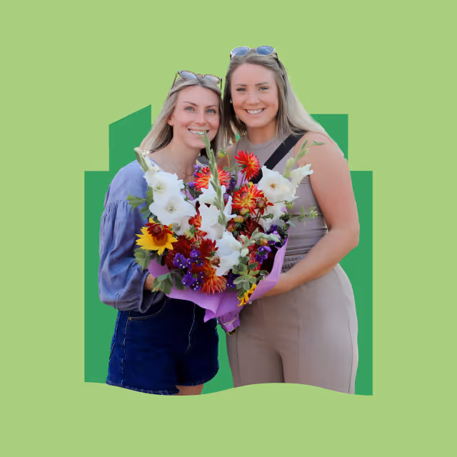 Two ladies holding flowers from the Neenah farmers market with Future neenah city scape shape behind them.