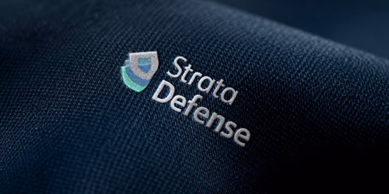 Close-up of dark fabric with embroidered Strata Defense logo featuring layered shield icon.