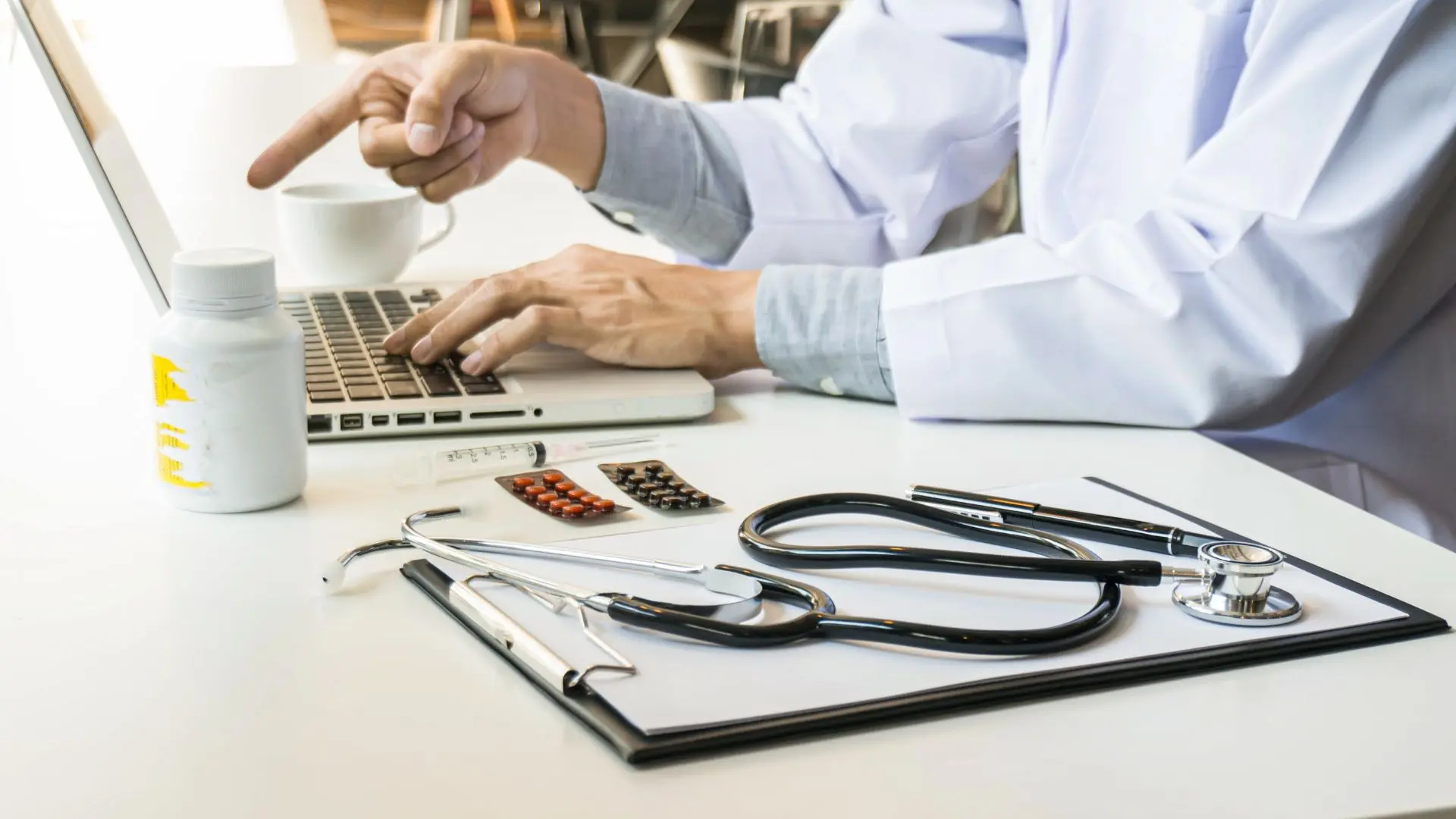 Doctor in a lab coat using a digital knowledge management system on a laptop to research treatment guidelines and patient data.