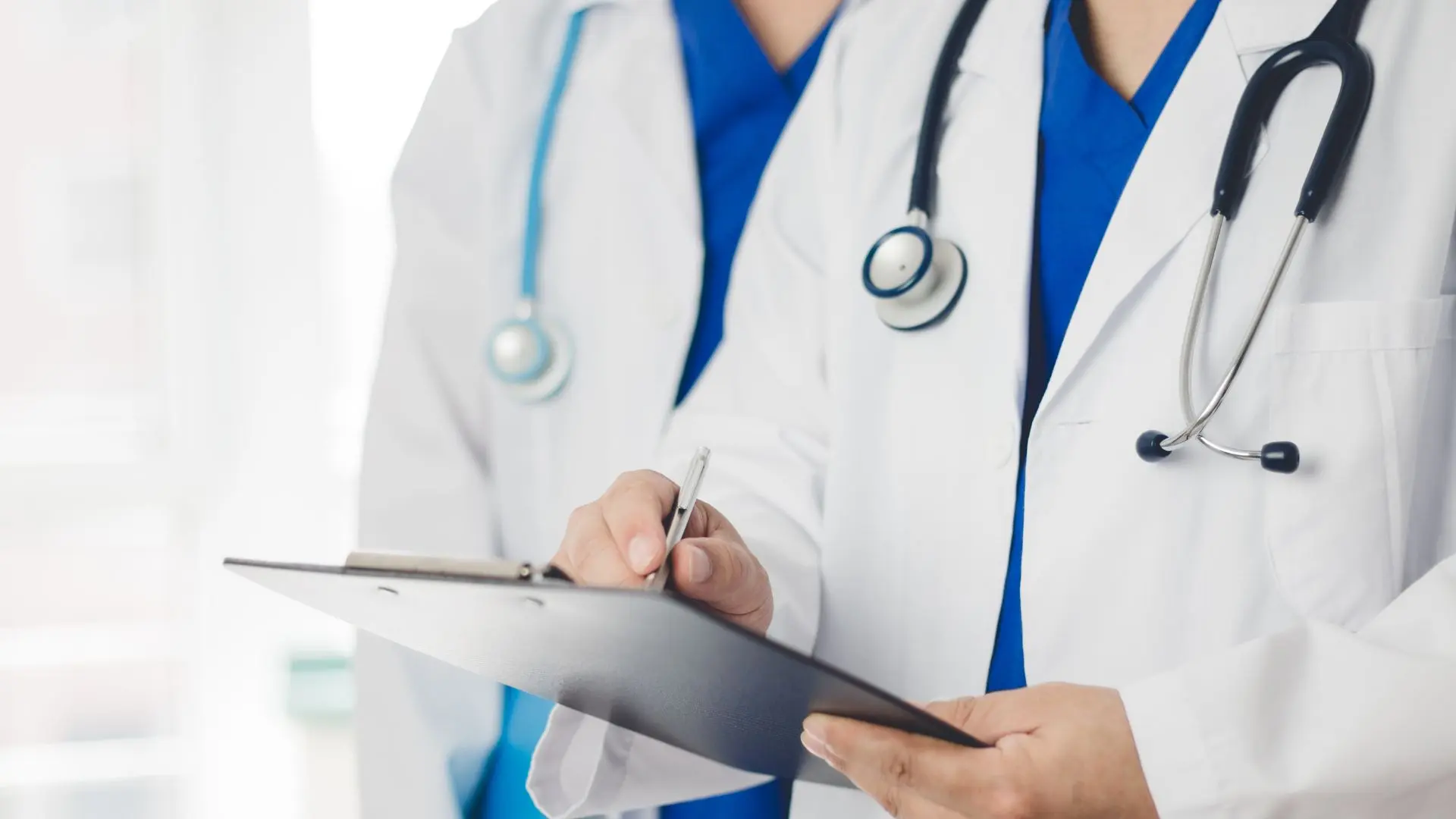 Two doctors in white coats with a stethoscope and clipboard during onboarding and documentation in a hospital, symbolizing successful physician recruitment.