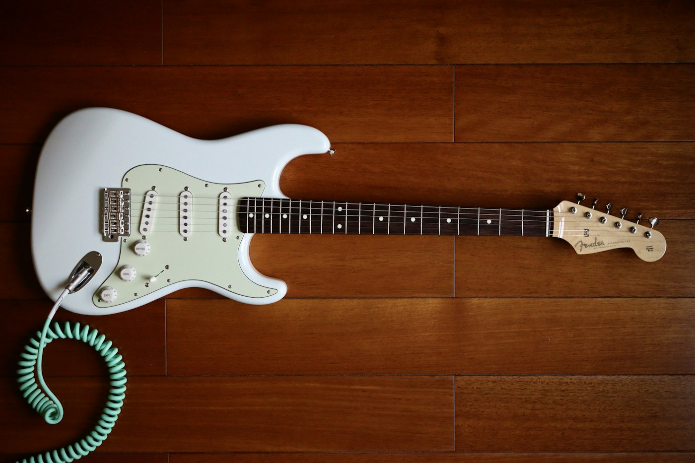 Valkoinen Stratocaster puulattialla: kolme yksikelaista mikrofonia, vibratalla ja kaareva runko