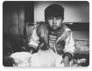 Black and white photo of a sad child in poor living conditions.