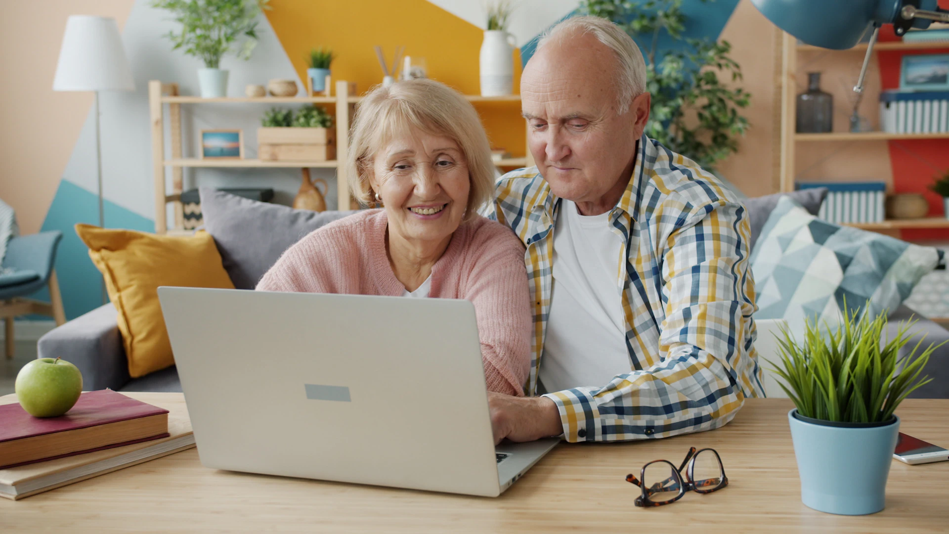 Elderly couple man ans woman are using computer at home talking typing enjoying internet content at home. Technology, people and lifestyle concept.