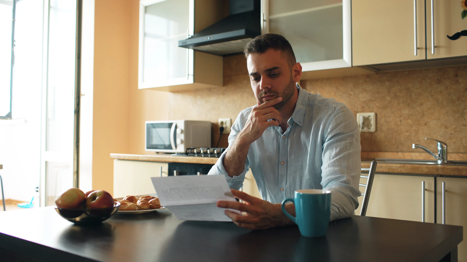 Upset young man reading letter with unpaid bill in the kitchen at home eraly morning