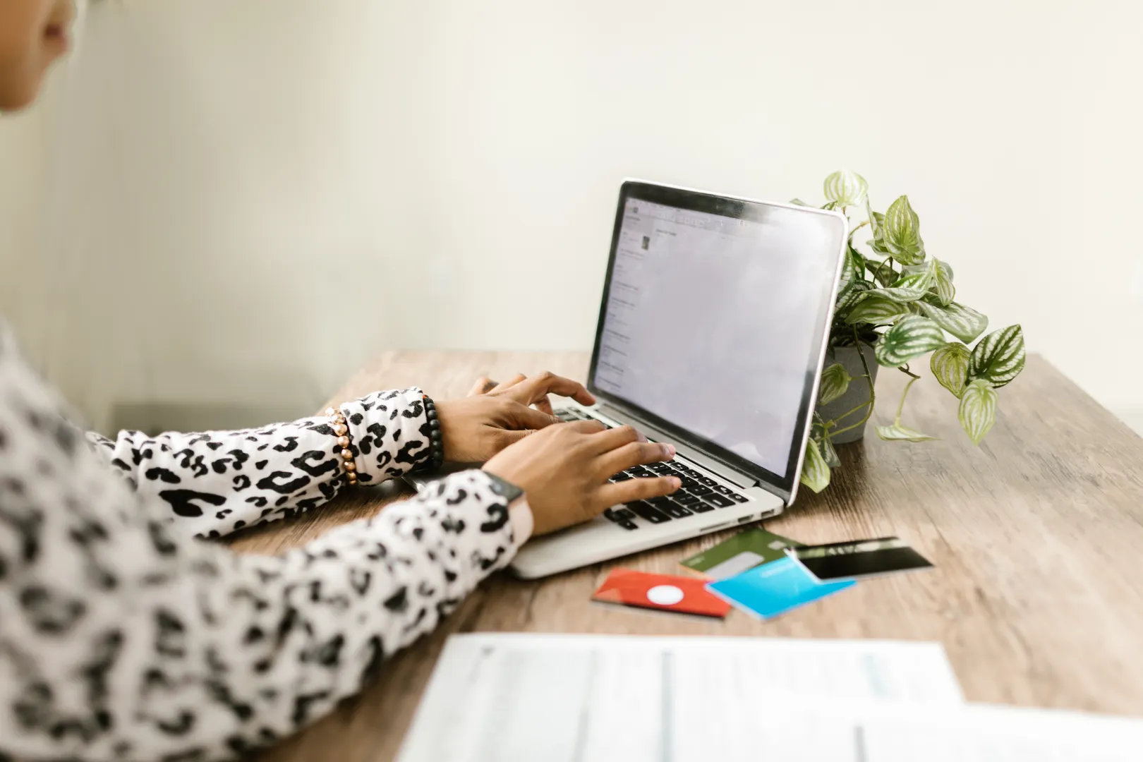 A close-up of hands typing on a laptop for online shopping with credit cards on a table.