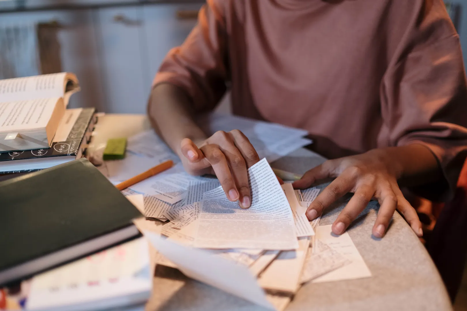 A young woman intensely studying with textbooks and notes scattered on a table.