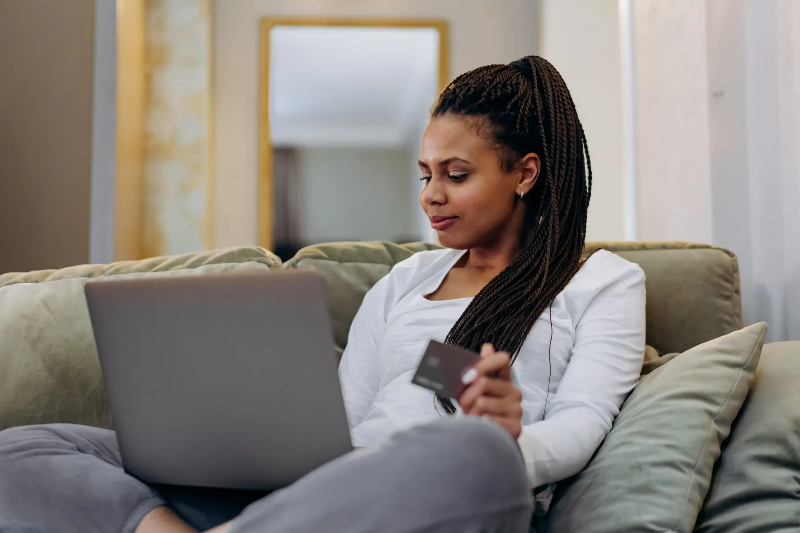 Woman sitting on a couch shopping online with a laptop and credit card.