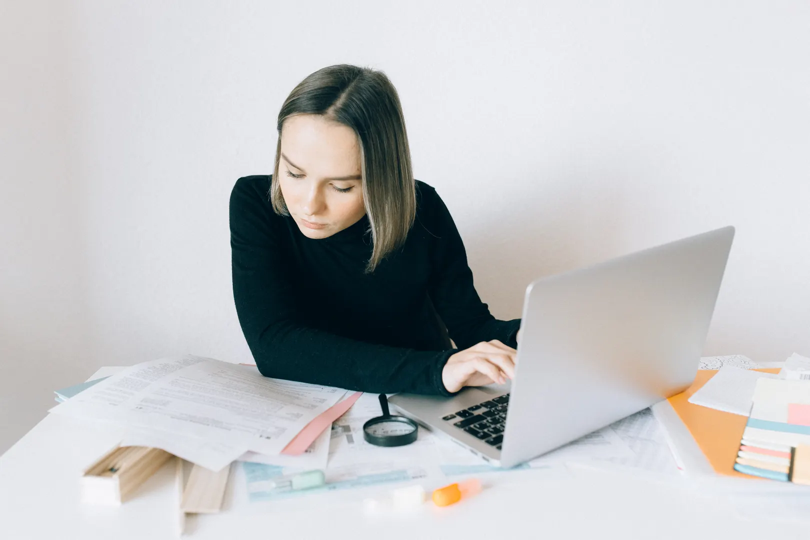 Focused woman researching on a laptop, surrounded by paperwork in a modern office.